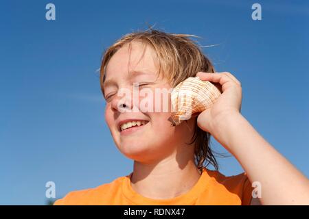 Portrait d'un jeune garçon à l'écoute d'une sea shell Banque D'Images