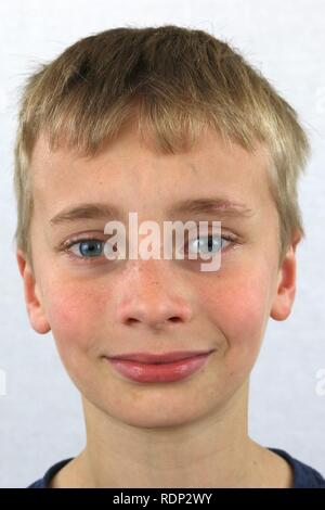Portrait d'un jeune garçon blond aux yeux bleus sur un fond blanc. Banque D'Images