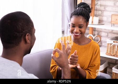 Smiling Young Couple Sitting on Sofa Communication avec les langues des signes Banque D'Images