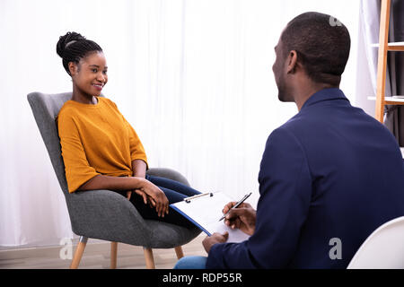 Jeune femme africaine assis près de psychologue avec presse-papiers pour traiter la dépression Banque D'Images