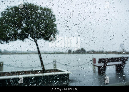 Gouttes de pluie sur le pare-brise un jour de pluie, des bancs sur le rivage d'un lac à l'arrière-plan Banque D'Images