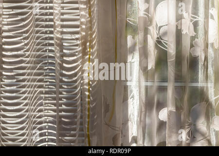 Les rayons de soleil font leur chemin à travers les stores fermés sur le rideau. Banque D'Images