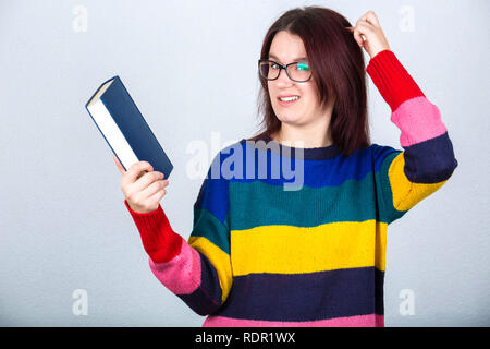 Young woman student holding a book et main pointée à la tête en essayant de se rappeler la connaissance accumulée et souvenirs. Banque D'Images