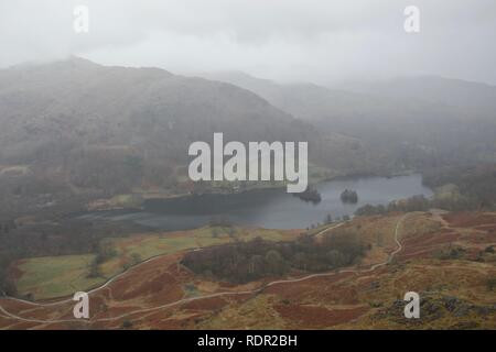 Vue de montagne (Loughrigg chuté) vers le bas sur le lac Rydal l'eau dans une vallée brumeuse, avec les autres montagnes disparaissant dans un brouillard de printemps. Col d'automne Banque D'Images