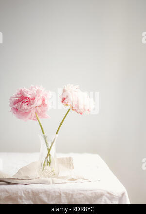 Deux pivoines rose en pleine floraison, sur une nappe de lin dans un vase de cristal Banque D'Images