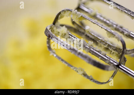 Un gros plan d'un batteur à main. Dans l'arrière-plan vous pouvez voir une pâte à gâteau jaune. La cuisson, délicieux gâteau fait maison. Le mélangeur est fait de métal. Banque D'Images