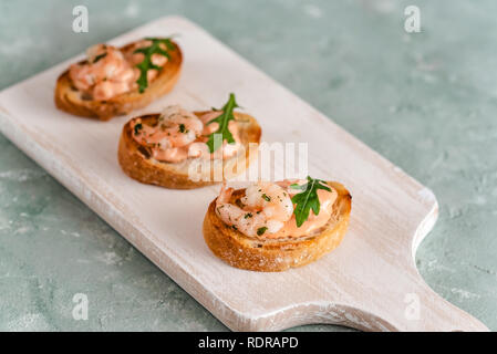 Bruschettas sandwiches aux crevettes, sauce crémeuse et salade de roquette. Banque D'Images