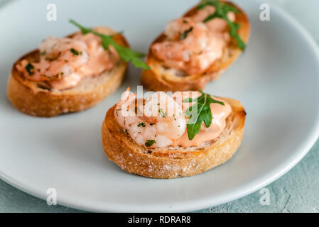 Bruschettas sandwiches aux crevettes, sauce crémeuse et salade de roquette. Banque D'Images