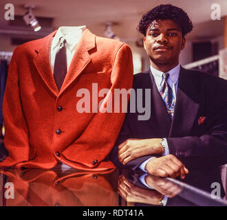 Un employé de magasin pose à côté d'un rouge élégant veste dans un magasin de vêtements haut de gamme à Manchester, Angleterre, Royaume-Uni en 1989. Banque D'Images