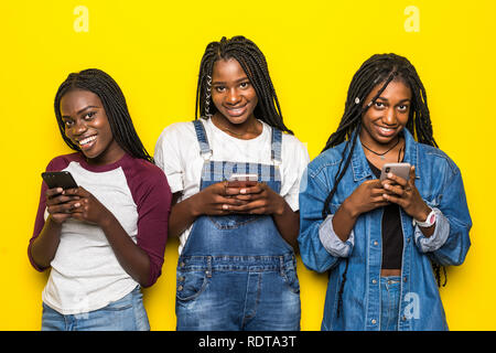 Trois jeunes filles africaines portant les tenues de l'utilisation de téléphones cellulaires les plus isolées sur fond jaune Banque D'Images