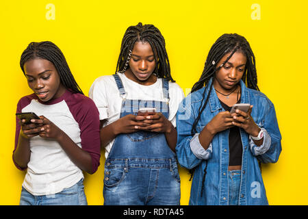 Trois jeunes filles africaines portant les tenues de l'utilisation de téléphones cellulaires les plus isolées sur fond jaune Banque D'Images