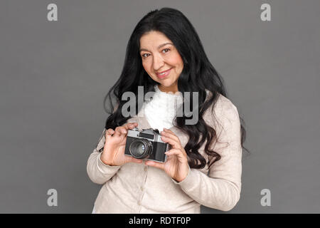 Photographe. Dame matures isolés sur des photos de gris avec caméra film espiègle sourire Banque D'Images