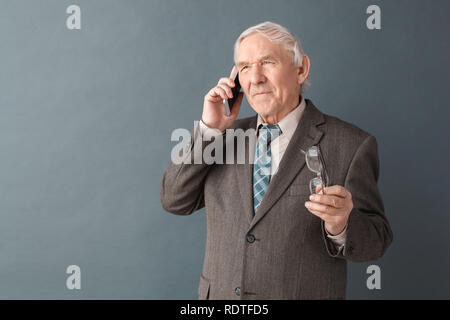 Man studio isolés sur gris holding glasses téléphone répondant à l'écoute d'appels concernés Banque D'Images