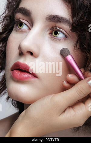 Make-up artist appliquer beauty maquillage sur le visage d'une belle jeune fille. Visagist avec brosse de maquillage à la main. Banque D'Images