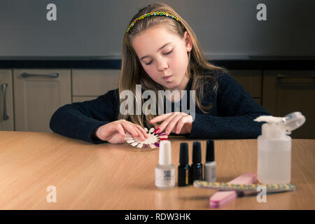 Portrait of cute 10 ans caucasien fille choisit la couleur de son vernis à ongles à la maison assis à la table de cuisine - verticale Banque D'Images