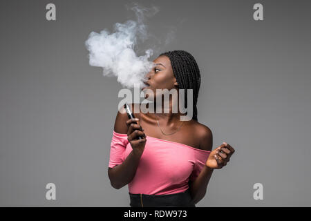 Vue de côté portrait de guy holding vape périphérique et exhalant nuage de fumée isolé sur fond bleu. Banque D'Images