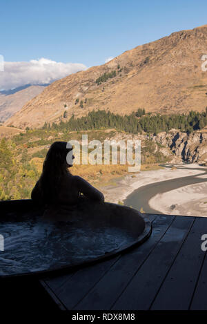 Une femme (Modèle 1992) relaxe dans un bain à remous tout en admirant la vue sur la Shotover River à l'Onsen Hot Pools près de Queenstown, en Nouvelle Zélande. Banque D'Images