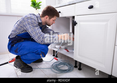 Jeune homme Nettoyage Plombier lavabo bouché dans la cuisine du tuyau Banque D'Images