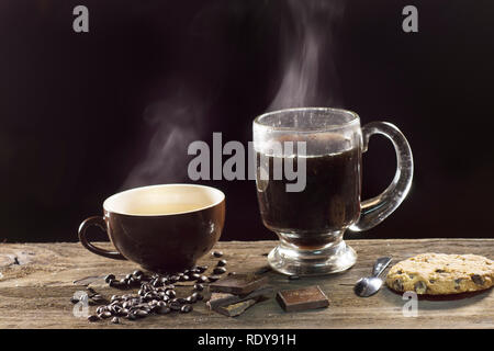 Deux tasses de café fumant sur le fond sombre, avec des grains de café et de chocolat Banque D'Images