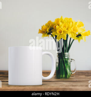 Mug blanc et vide à côté d'un vase de jonquilles. Parfait pour les entreprises qui vendent des tasses, incrustation juste votre devis ou sur la conception de l'image. Banque D'Images