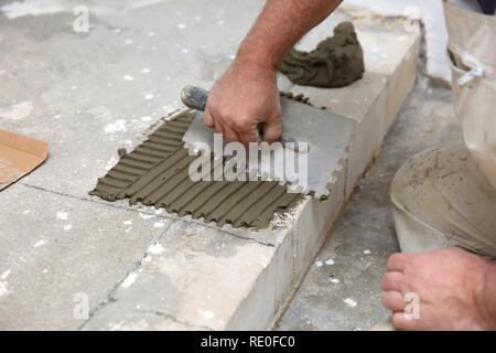 Le travailleur de la construction s'étend uniformément la surface de l'escalier avec du ciment masse adhésive à l'aide d'un outil à main. Banque D'Images