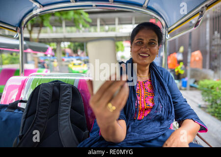 Indienne mature woman sitting in tuk tuk et using mobile phone Banque D'Images