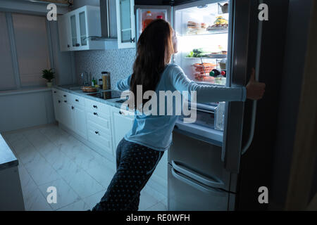 L'ouverture de porte du réfrigérateur femme avec divers aliments dans la cuisine Banque D'Images