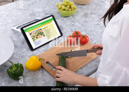 Coupe femme Concombre avec couteau de cuisine près de recettes de cuisine sur écran de tablette numérique Banque D'Images