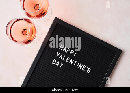 Le jour de la Saint-Valentin. Letterboard noir avec citation Happy Valentine's Day, et verre de vin rose sur fond rose. Banque D'Images