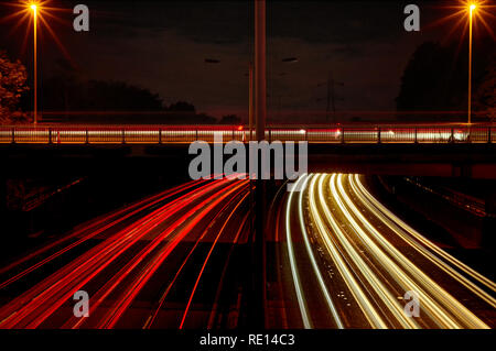 Véhicule rouge et blanc tout en légèreté comme UK d'autoroute le trafic passe un pont dans les deux directions, de sentiers de plus de véhicules sont vus sur le pont. Banque D'Images