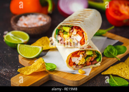 Burritos au poulet grillé enveloppements, haricots, maïs, tomates et avocat, sur une planche en bois, un arrière-plan sombre. Burrito la viande, la nourriture mexicaine. Banque D'Images