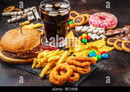 Junk Food concept. Fond d'aliments malsains. Restauration rapide et le sucre. Burger, bonbons, chocolat, chips, beignets, soda sur un fond sombre. Banque D'Images