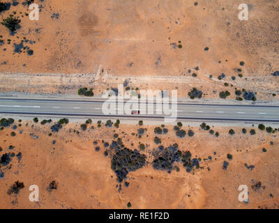 Vue aérienne d'une voiture rouge solitaire conduisant sur une route droite à travers un paysage désertique Banque D'Images