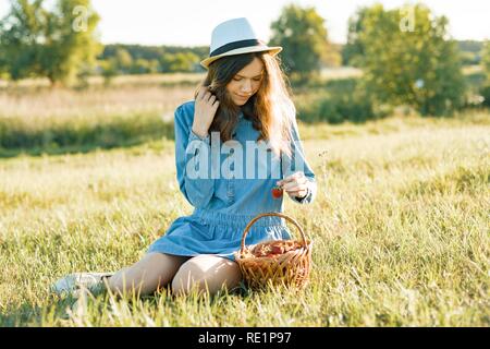 Jolie teen girl eating strawberry. Arrière-plan de la nature, paysage rural, vert prairie, country style. Banque D'Images