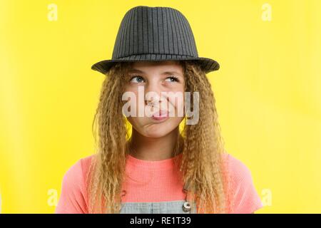 Jolie Fille 12-13 ans, blonde, aux cheveux bouclés dans un chapeau, l'air songeur de côté, en pensant à l'école. Concept d'expressions du visage, jaune backgrou Banque D'Images