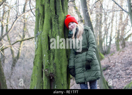 Jeune femme en tenue d'hiver leaning against tree in forest Banque D'Images