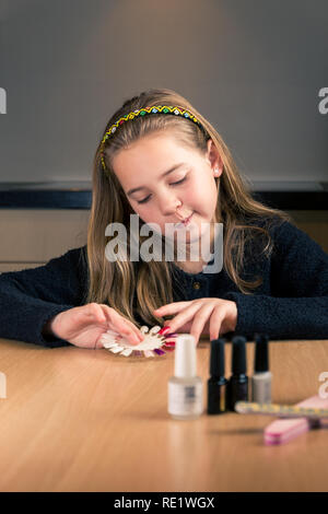 Portrait of cute 10 ans caucasien fille choisit la couleur de son vernis à ongles à la maison assis à la table de cuisine - verticale Banque D'Images