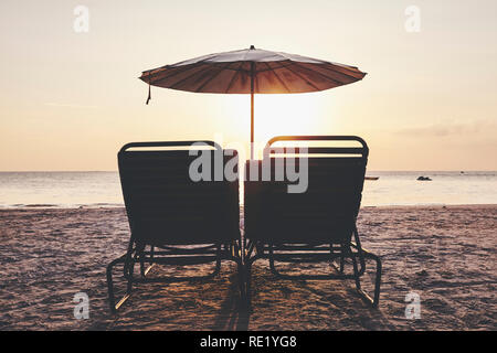 Chaises et parasol de plage vide silhouettes au coucher du soleil, aux teintes de couleur photo. Banque D'Images