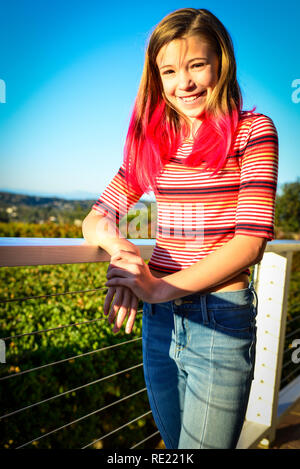 Tween heureux avec des cheveux rose, sourit tout en se penchant sur le balcon à l'extérieur du rail au coucher du soleil Banque D'Images
