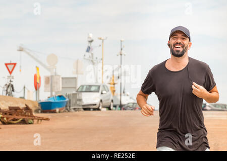 Portrait d'un homme avec la barbe d'exécution sur la rue parlant avec un casque sans fil - écouteurs. Banque D'Images