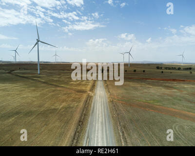 Vue aérienne d'un parc éolien avec plusieurs turbines le long d'un chemin de terre au milieu d'un champ sec sous un ciel dégagé Banque D'Images