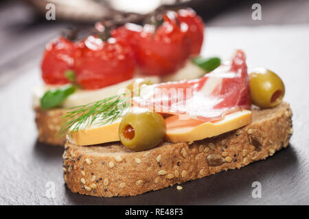 Libre de bruschetta avec fromage à la crème, tomate cerise, basilic, fromage, jambon fumé, olives sur une table en bois. Banque D'Images