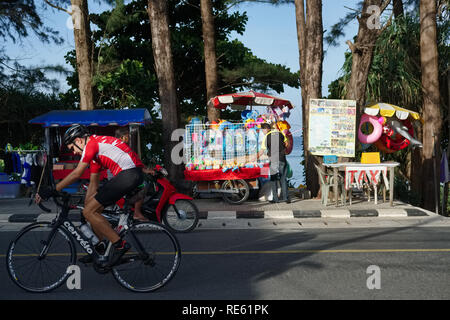 Un cycliste de l'équitation à travers Nai Thon, Phuket, Thaïlande ; dans le b/g services touristiques et plage de Nai Thon Banque D'Images