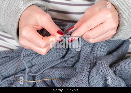 Femme avec les mains manucure tricoter un chandail gris avec des aiguilles à tricoter, close-up Banque D'Images