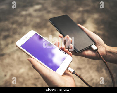 La main de l'holding smartphone blanc chargement de la batterie de l'alimentation externe bank dans l'air extérieur Banque D'Images