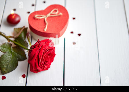 Frais unique rose rouge fleur sur la table en bois blanc avec des paillettes en forme de coeur saupoudré autour, de bougies et de cadeaux dans la boîte. Concept d'amour ou de Valentines Banque D'Images