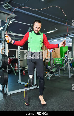 Muscular beau jeune homme barbu avec prothèse de jambe remise en forme portant des vêtements de sport faisant sauter l'exercice dans la salle de sport moderne Banque D'Images