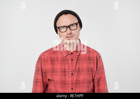 Jeune homme européen en chemise rouge insatisfait fronce et attend sullenly. Banque D'Images