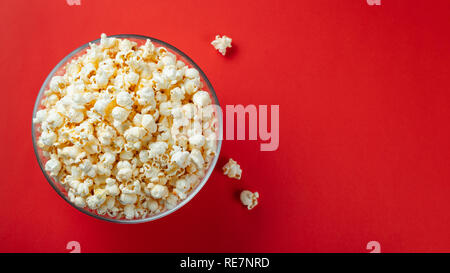 Bol en verre de popcorn salé sur un fond rouge. Vue de dessus avec l'exemplaire de l'espace. Mise à plat. Banque D'Images