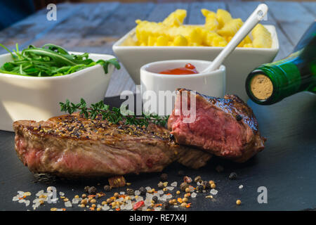 Steak grillé avec frites et servi sur plaque de pierre noire sur table en bois. Banque D'Images